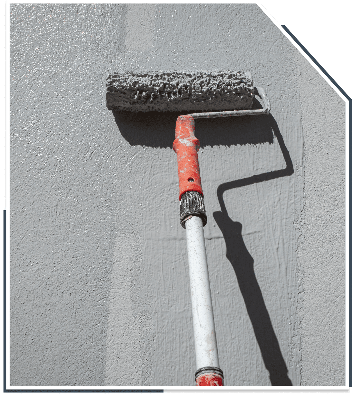 A paint roller with a red handle applies light gray paint to a textured wall.