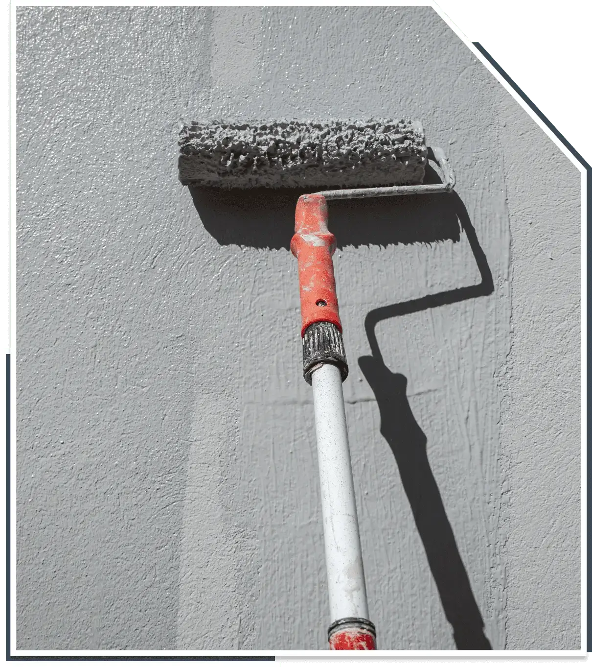 A paint roller with a red handle applies light gray paint to a textured wall.